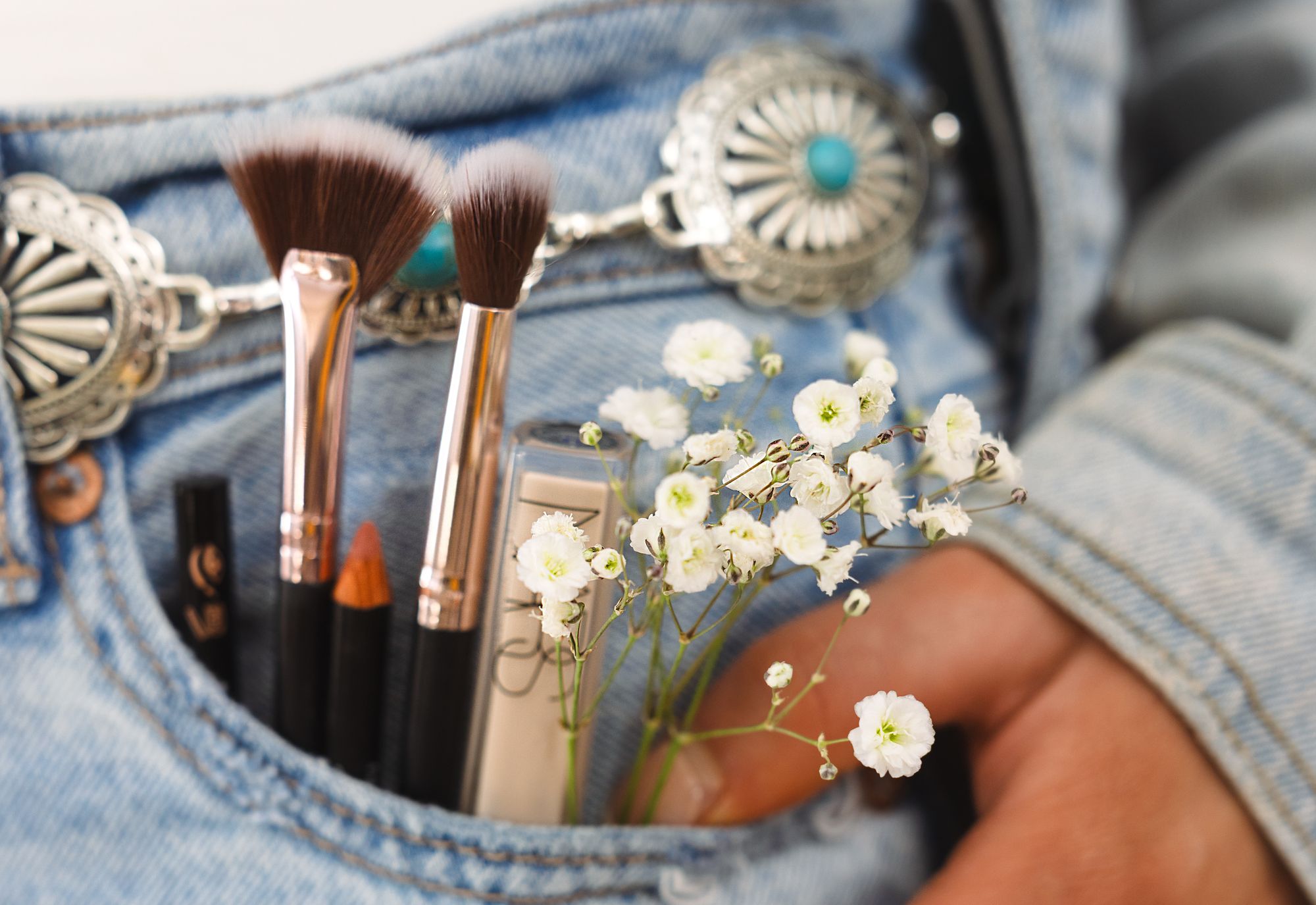 Makeup brushes and baby's breath tucked in a denim pocket